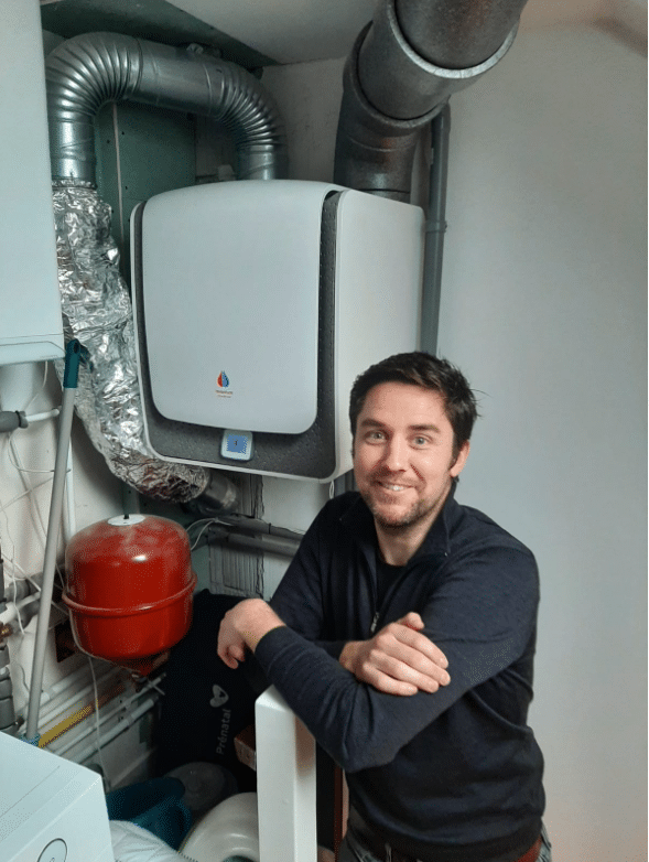 een man poseert voor een heetwaterinstallatie en kijkt lachend in de camera