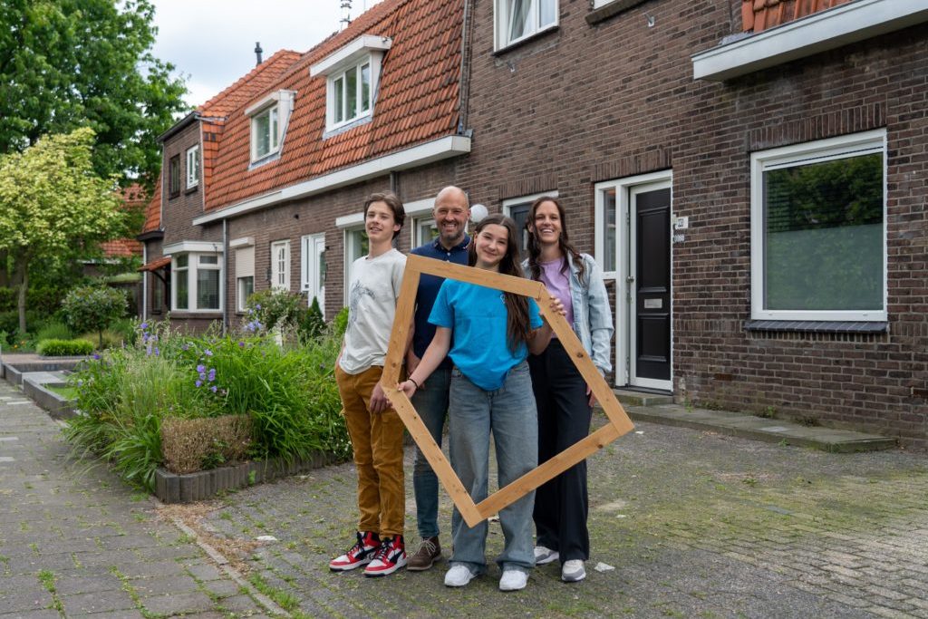 Duurzame-Huizen-Route-5-1024×718 een groep mensen staat op straat met een houten frame in de vorm van een huis