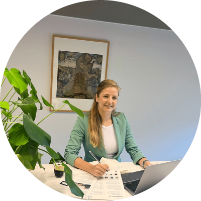 circular_image_optimized_2000 een vrouw zit aan een bureau met een laptop erop, en kijkt lachend in de camera
